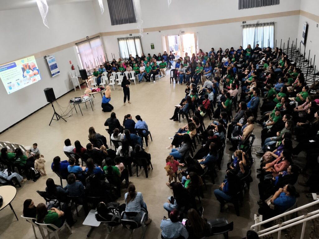 Treinamento de primeiros socorros com simulação de RCP e slide informativo projetado ao fundo